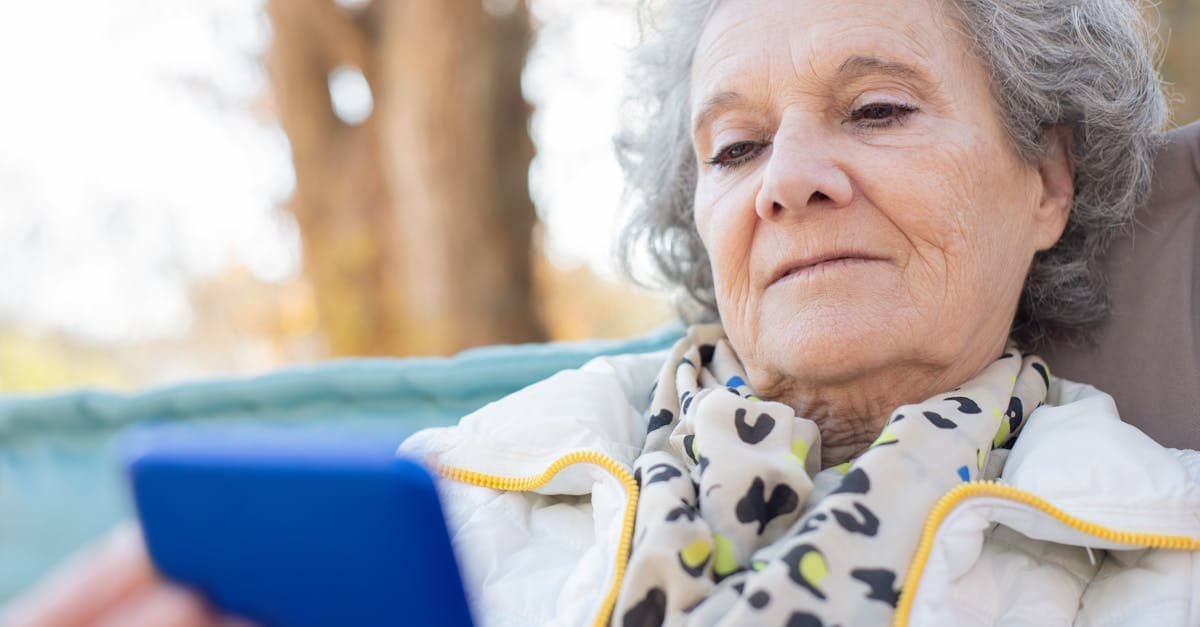 Elderly woman with a smartphone relaxing outdoors in autumn.